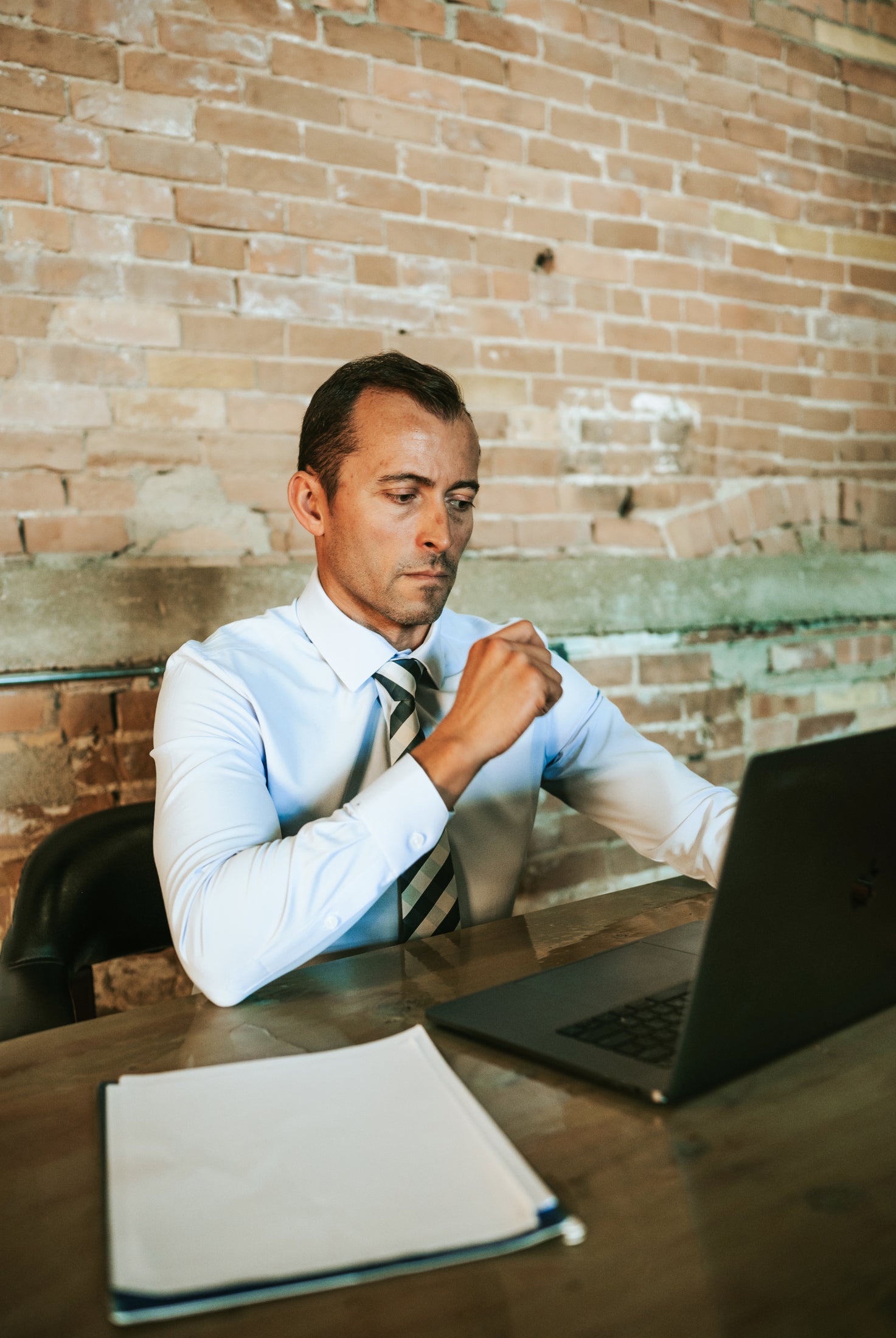 Man dressed in mens business clothes doing work on his laptop at his desk