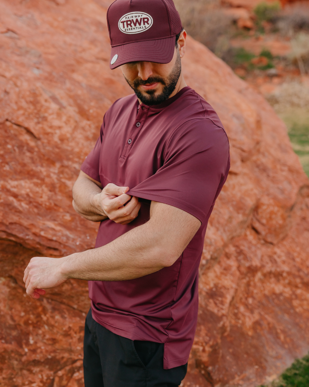 Man wearing a maroon shirt and cap with 'TRWR' logo against a rocky background