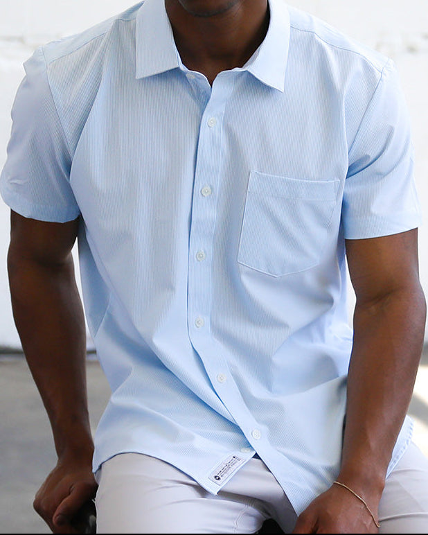 Man wearing a light blue shirt sitting against a white wall.